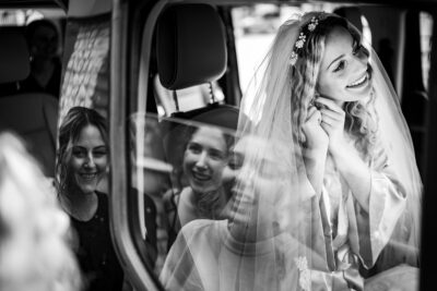 Menyasszony utolsó simításai a kocsiban, miközben a koszorúslányok nézik