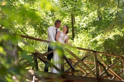 Menyasszony es vőlegény egymásra néznek az erdőben egy fa hídon